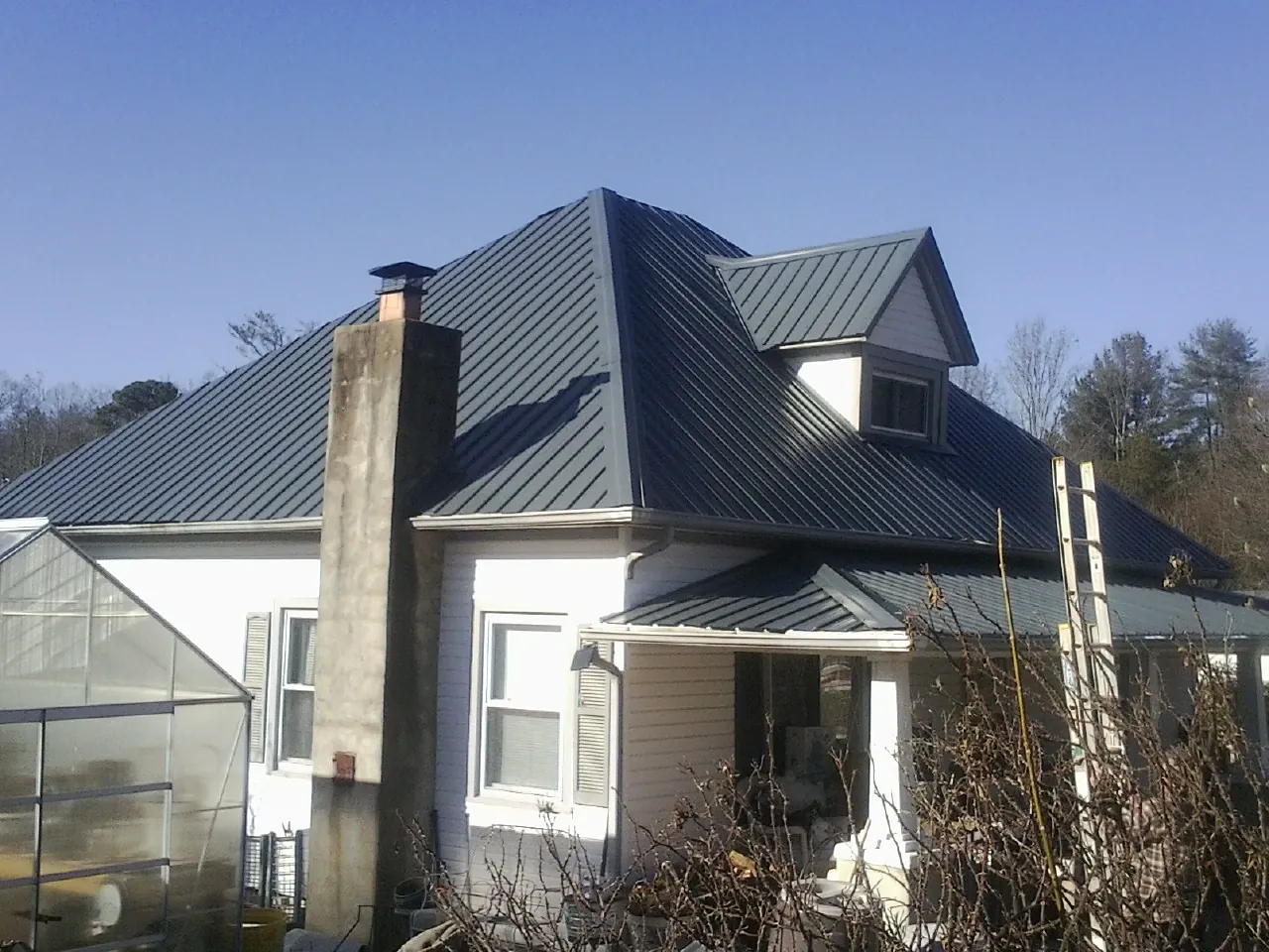 Dark blue standing seam metal roof on a white farmhouse with dormer — Slate & Tile Roof Repair by Roofing Brothers in Gibbon Glade