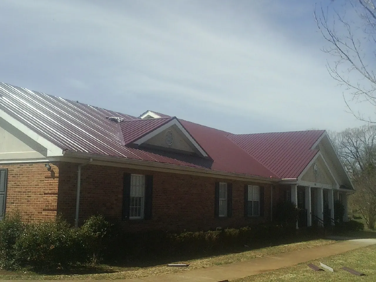 Red metal roof with gabled entries on a long brick building, from a Hail Damage Roof Repair job in Gibbon Glade