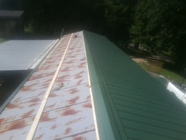 Old rusted panels beside newly installed green metal roofing — Wind Damage Roof Repair by Roofing Brothers in Gibbon Glade