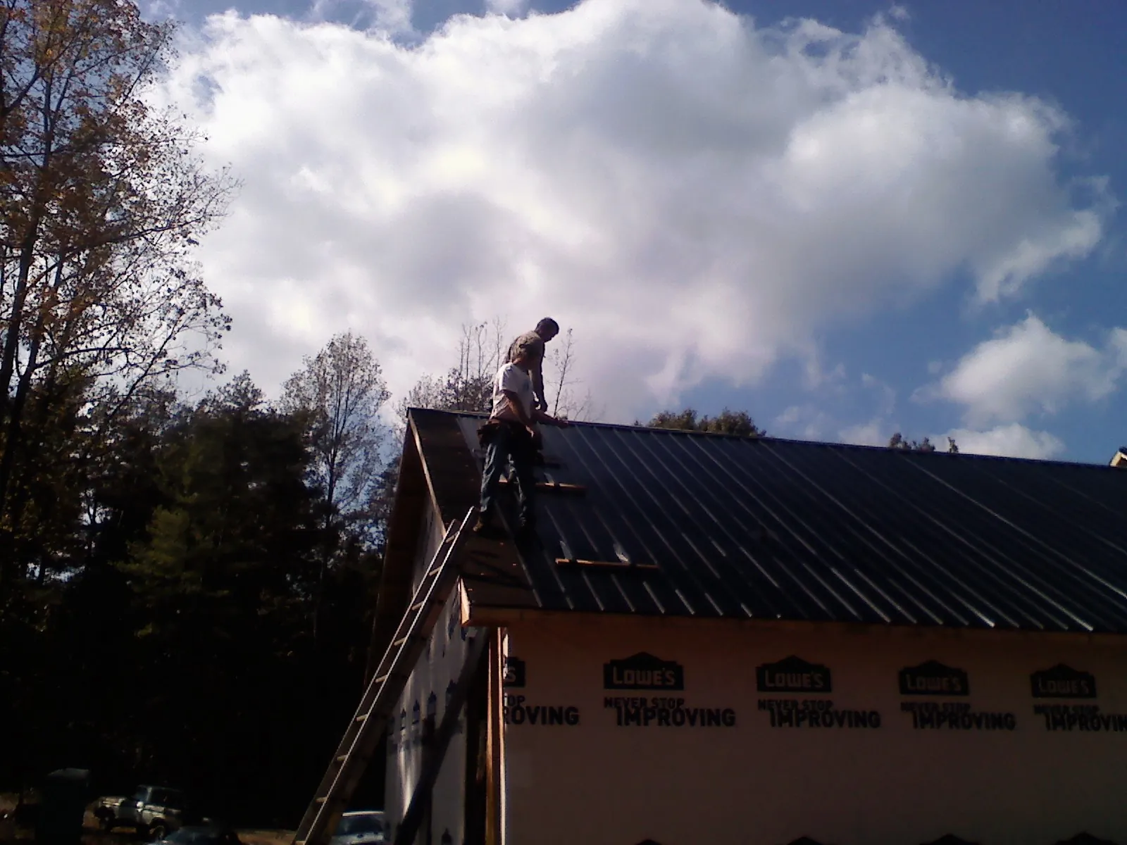 Roofer fastening dark metal panels high against a cloudy sky, from a Roof Inspection job in Gibbon Glade