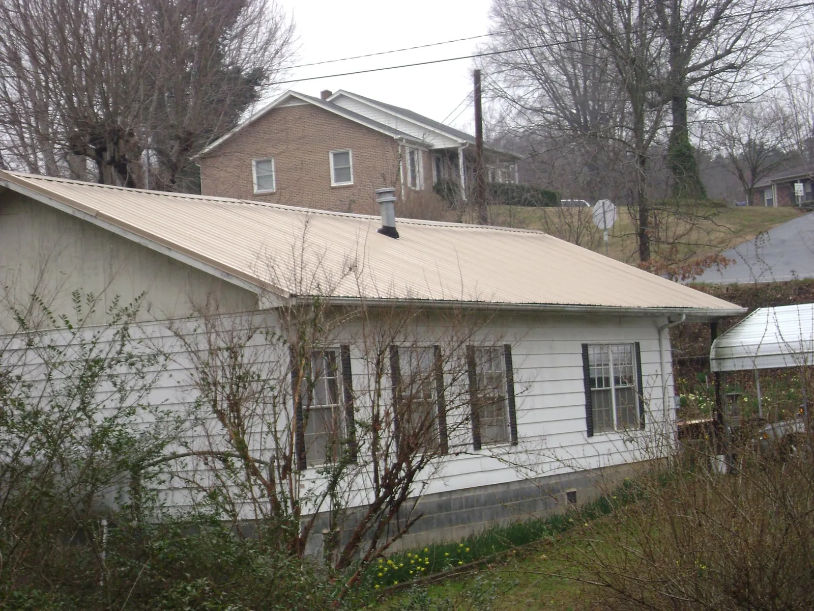 Tan metal roof on a white sided house set into a hillside — Commercial Roofing by Roofing Brothers in Gibbon Glade