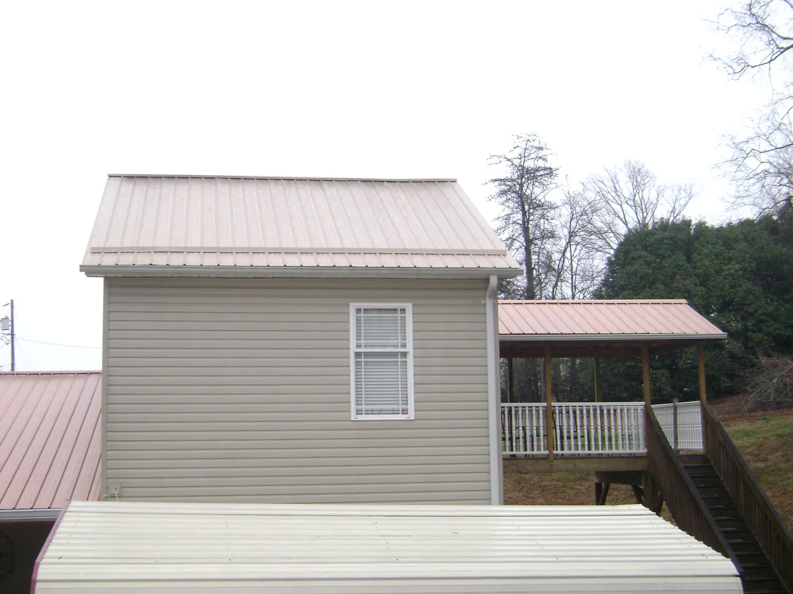 Tan metal roofs on a two story addition and attached porch, from a Roof Replacement job in Gibbon Glade